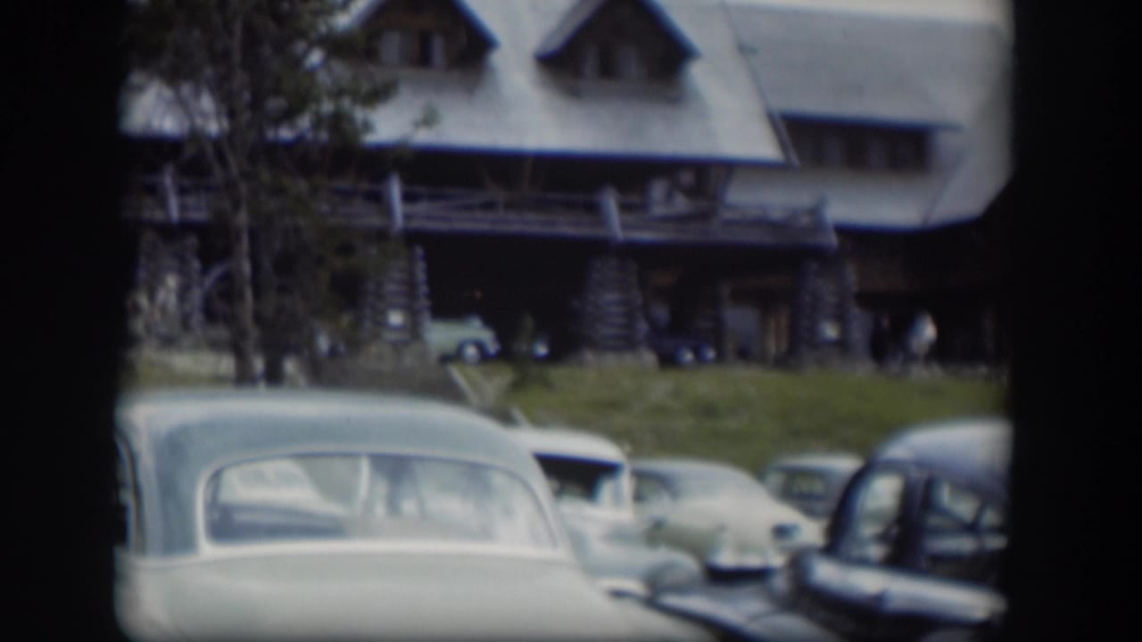Classic cars parked in front of a rustic log-style building with dormer windows.