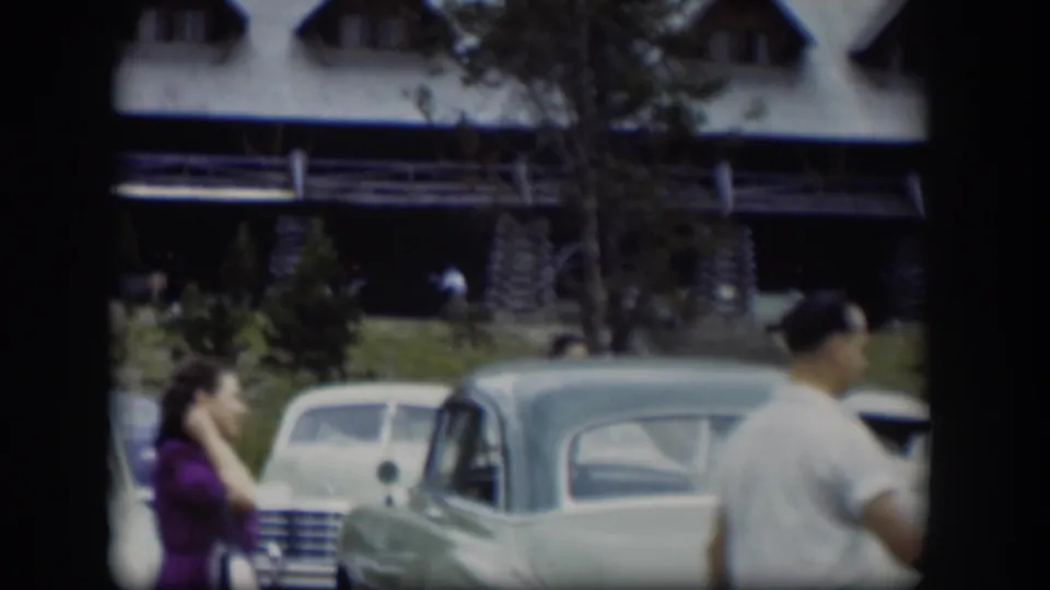 1951 Wyoming 8mm frame with adults crossing the foreground near mid-century cars and a log-style building.