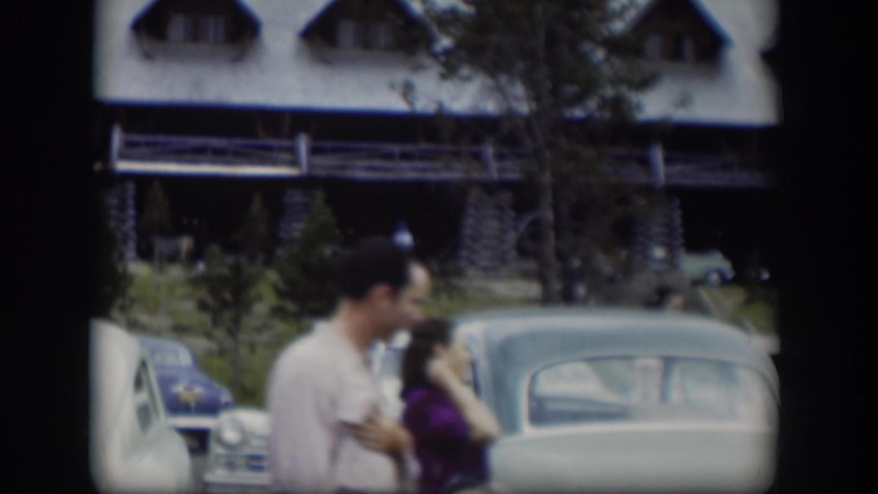 In 1951 Wyoming footage, two adults walk past rounded parked cars outside a large log cabin-style lodge.