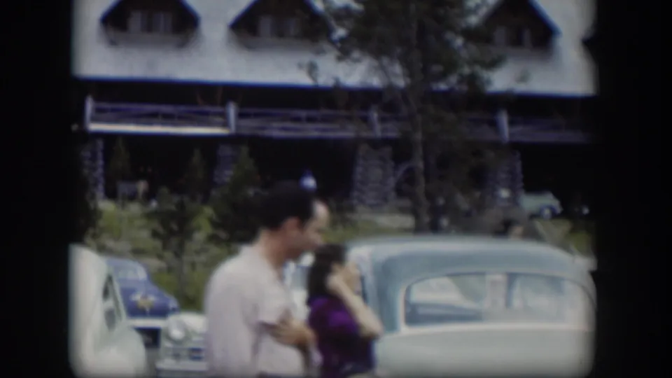 In 1951 Wyoming footage, two adults walk past rounded parked cars outside a large log cabin-style lodge.