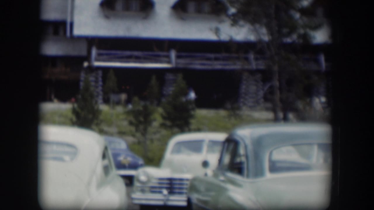 Classic cars parked on grass outside a large lodge building.