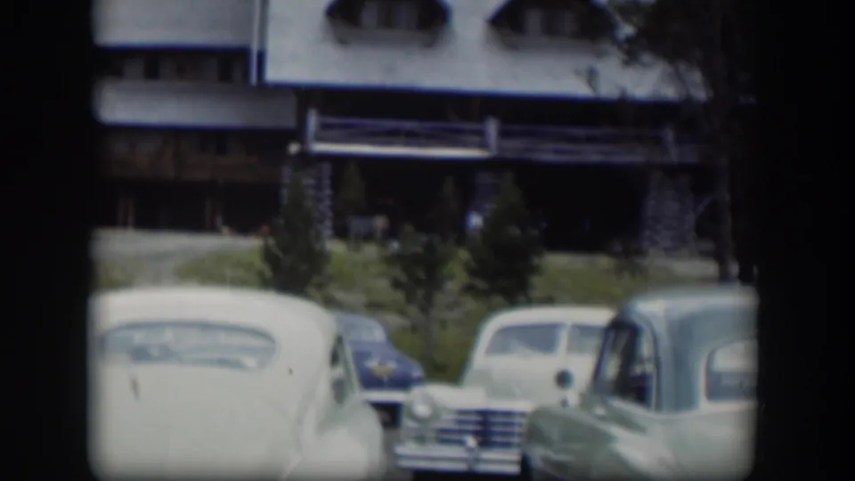 A soft 8mm view shows classic cars in the foreground and a large log lodge beyond them in Wyoming.