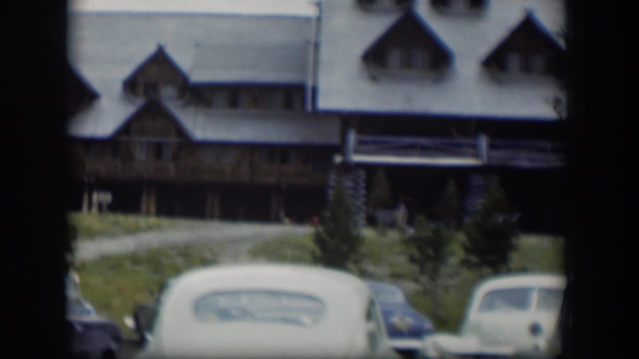 Rustic log lodge with pale gabled roofs and parked rounded cars in front.
