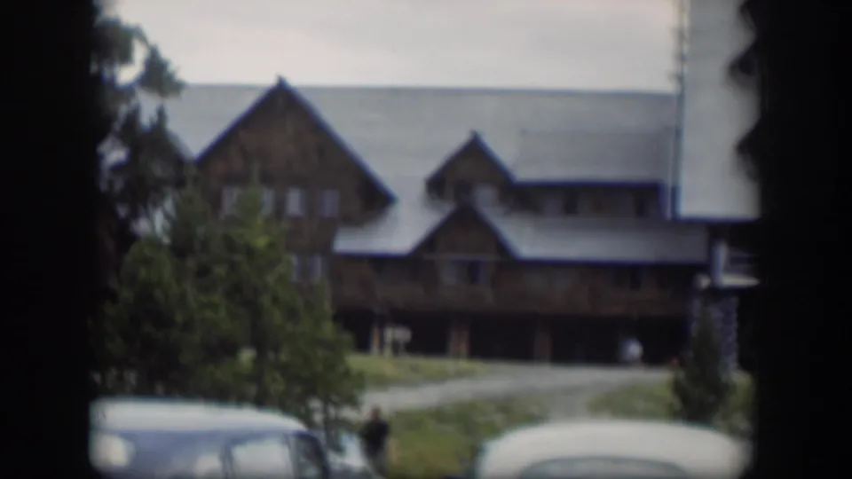 1951 Wyoming 8mm frame showing the lodge, parked cars, trees, gravel drive, and a small distant person near the lower center.