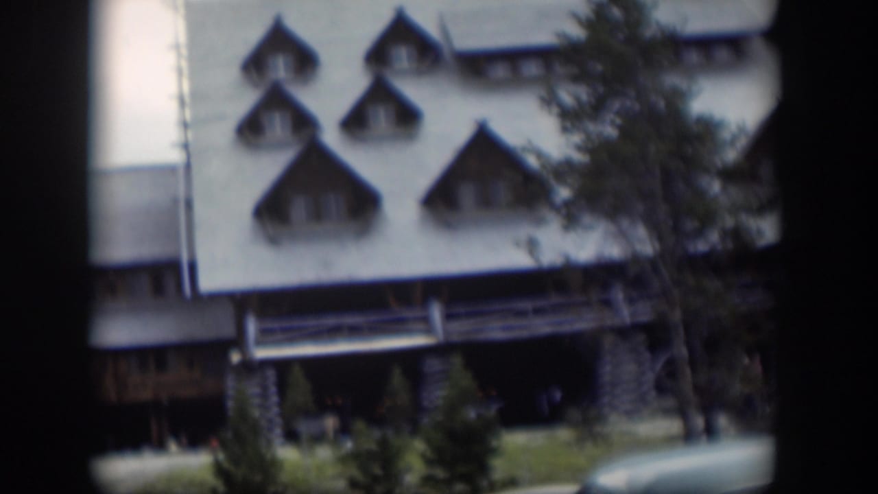 White building facade with pointed dormer windows, trees, and dark frame borders.