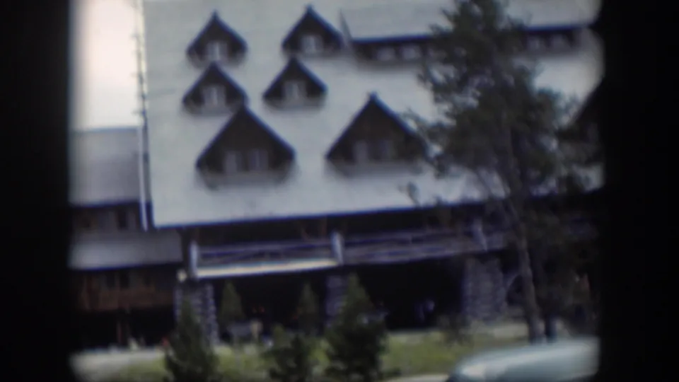 1951 Wyoming 8mm frame showing a white building with steep triangular dormers, evergreen trees, and dark film-gate edges.