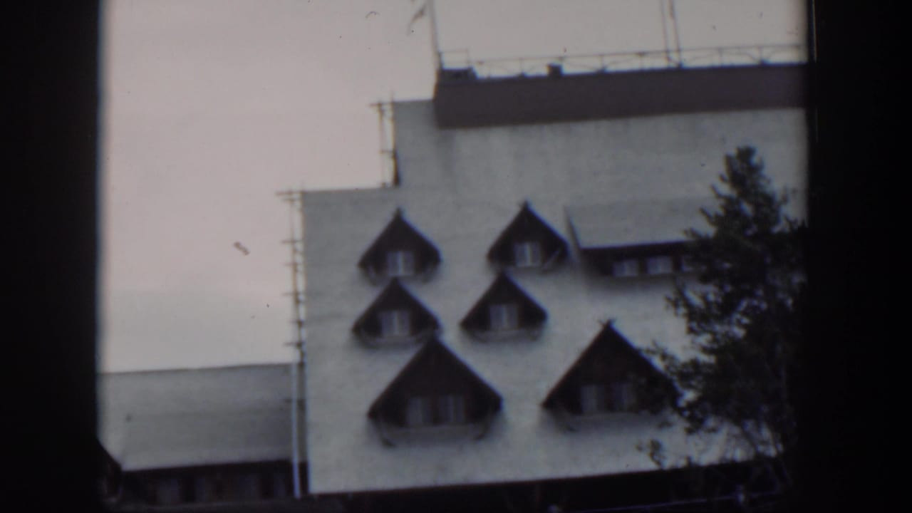 1951 Wyoming 8mm frame showing the upper facade, multiple pointed dormers, rooftop railing, and evergreen branches.