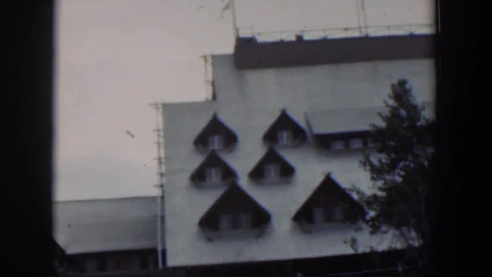 1951 Wyoming 8mm frame showing the upper facade, multiple pointed dormers, rooftop railing, and evergreen branches.