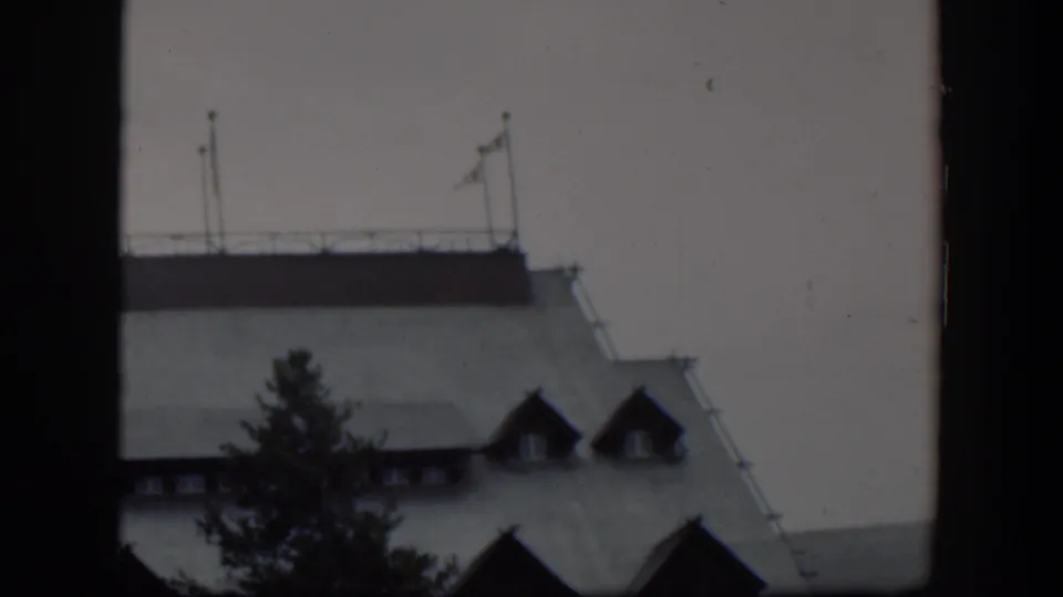 1951 Wyoming 8mm frame showing a pale steep roof, dark dormers, and a foreground tree within heavy film gate borders.