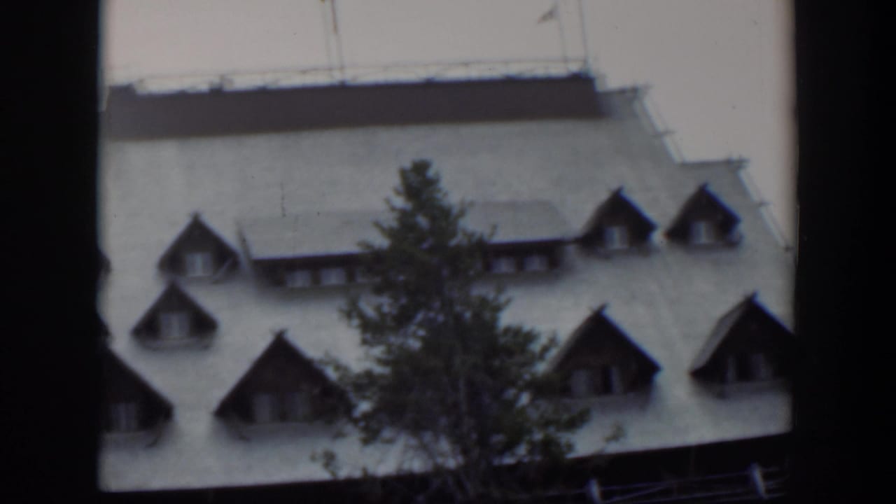 1951 Wyoming 8mm frame showing more of the large building roof, dormers, and tree during the upward camera movement.