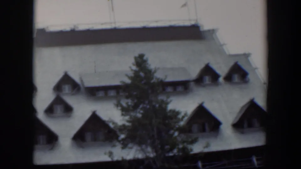 1951 Wyoming 8mm frame showing more of the large building roof, dormers, and tree during the upward camera movement.