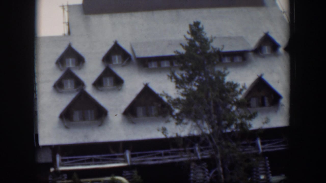 1951 Wyoming frame revealing the building exterior with dormers, railings, a pale roof, and a foreground tree.