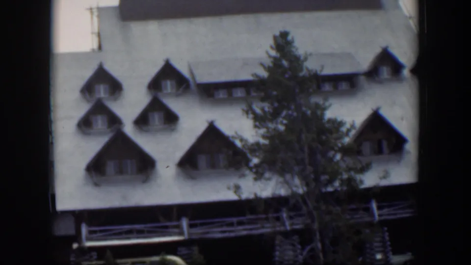 1951 Wyoming frame revealing the building exterior with dormers, railings, a pale roof, and a foreground tree.