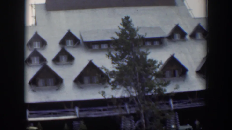 1951 Wyoming home-movie frame showing a rustic lodge roof, dormer windows, porch edge, and evergreen tree.