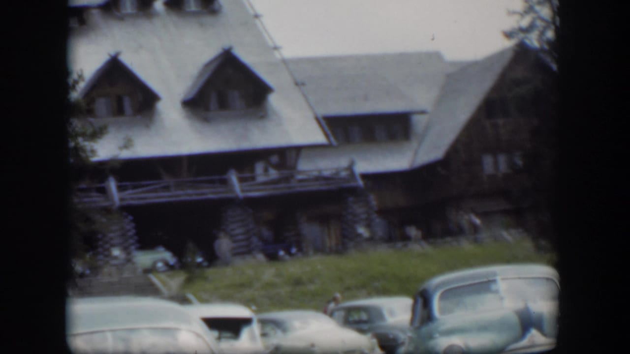 1951 Wyoming frame showing the rustic lodge, lawn, several parked classic cars, and distant people by the entrance.