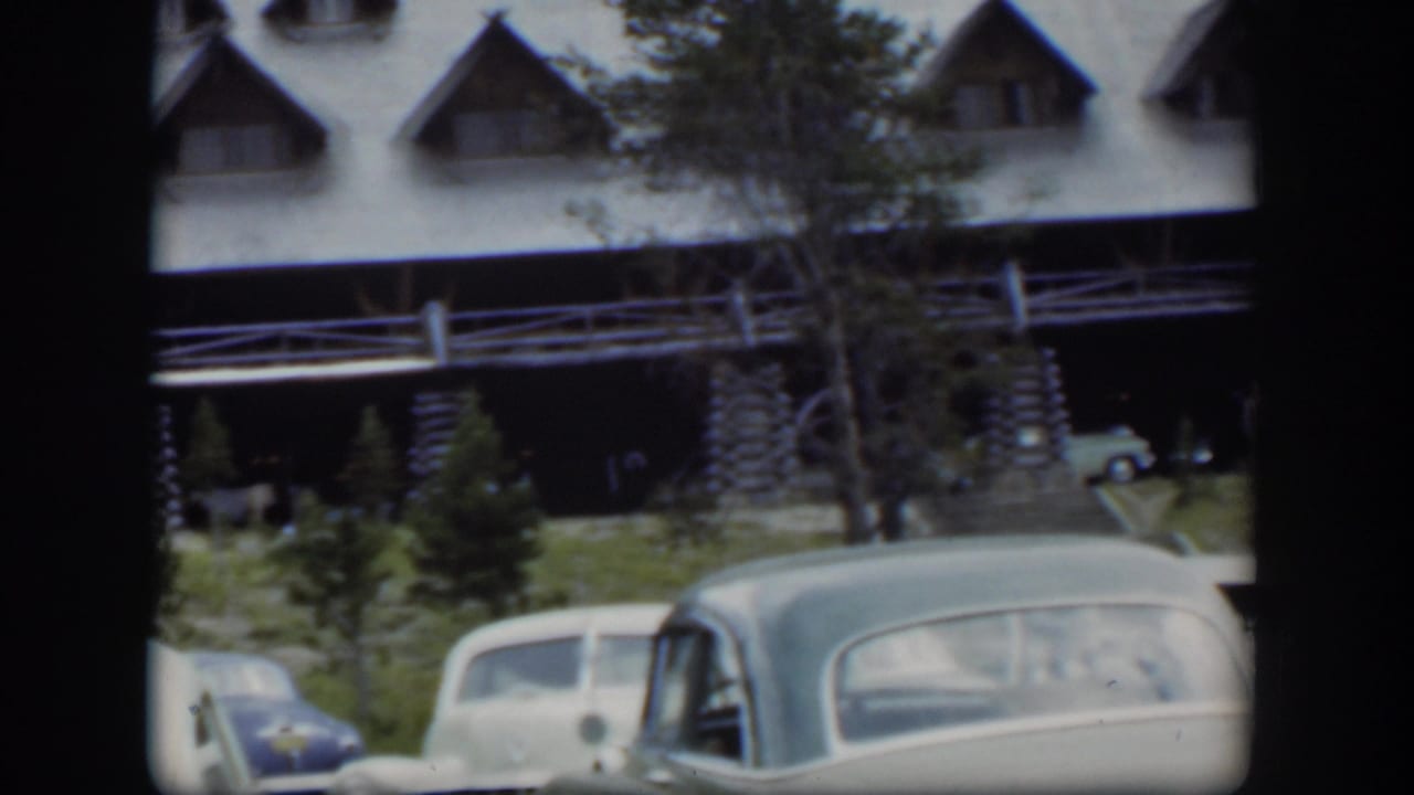 1951 Wyoming home-movie view of parked cars below a rustic lodge porch, with trees and dormer windows in soft 8mm focus.