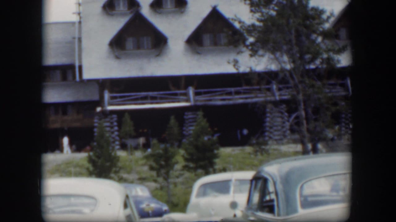 1951 Wyoming frame showing two parked cars below a stone-and-log lodge facade with dormer windows and trees nearby.