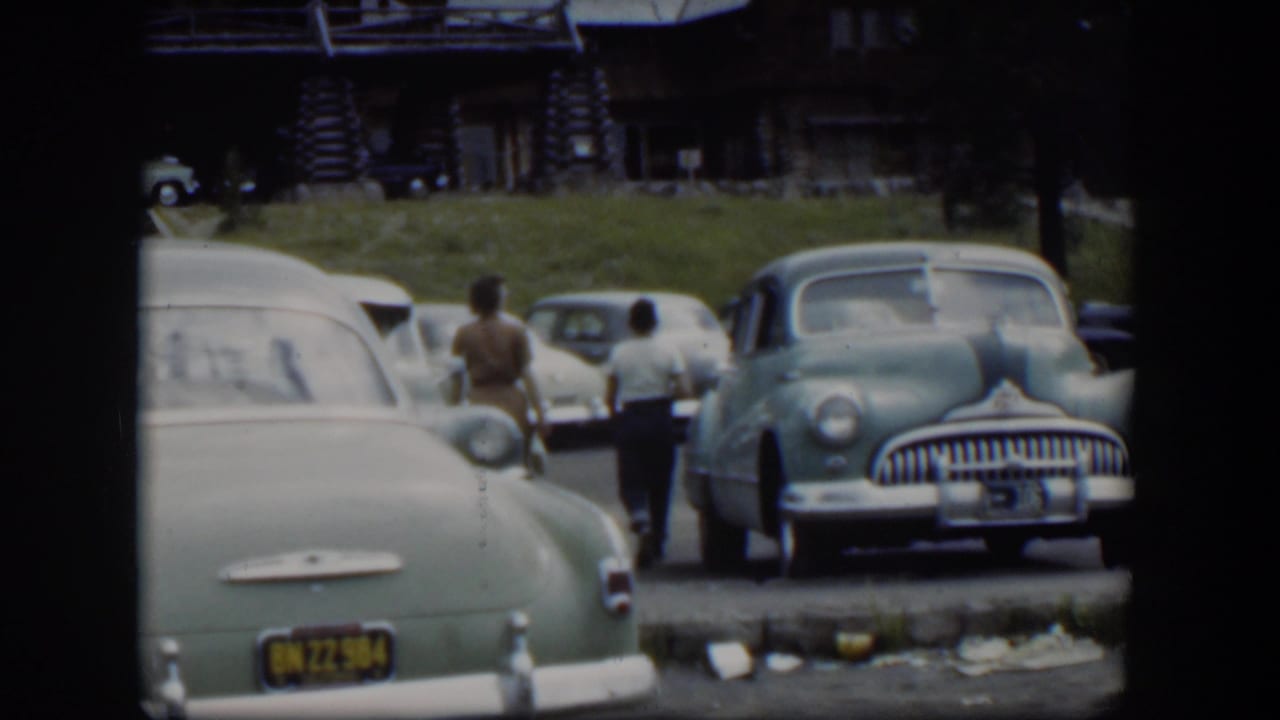 In the Wyoming home-movie scene, the woman and boy continue past a row of parked 1950s cars toward the lodge area.