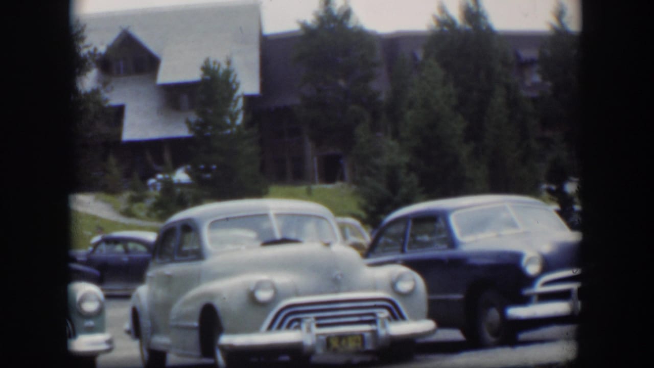 1951 Wyoming 8mm view of parked mid-century automobiles with chrome fronts, trees, grass, and a lodge-style exterior behind them.
