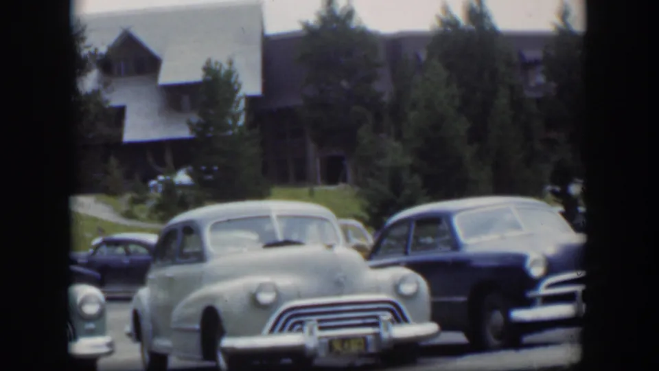 1951 Wyoming 8mm view of parked mid-century automobiles with chrome fronts, trees, grass, and a lodge-style exterior behind them.