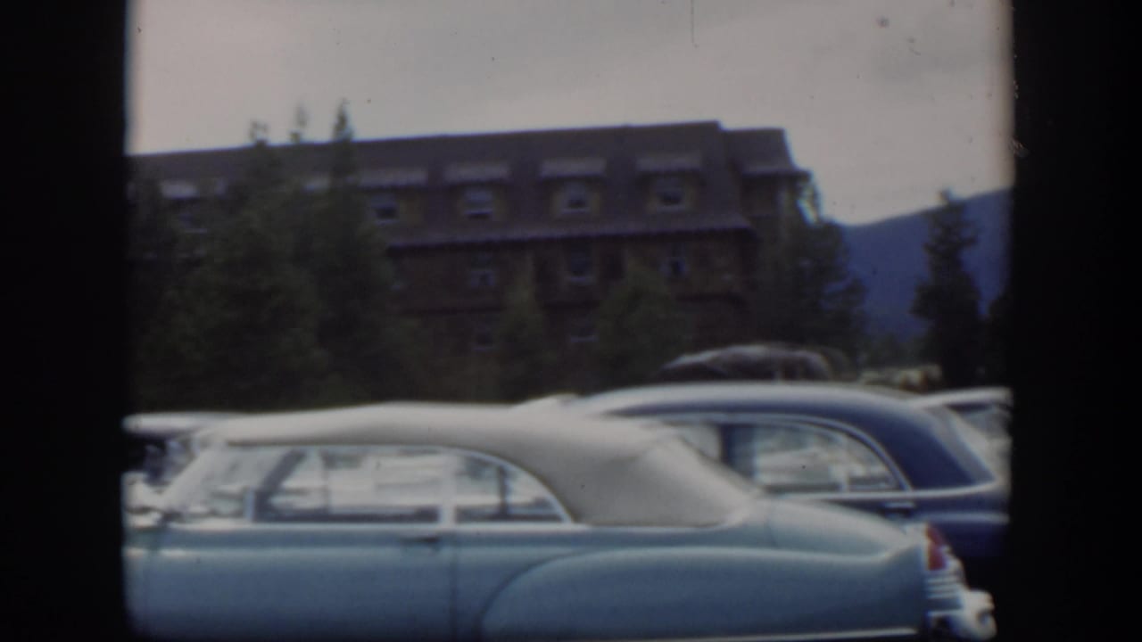 1951 Wyoming 8mm frame with a pale mid-century car in the foreground and a lodge, evergreens, and mountain backdrop beyond.