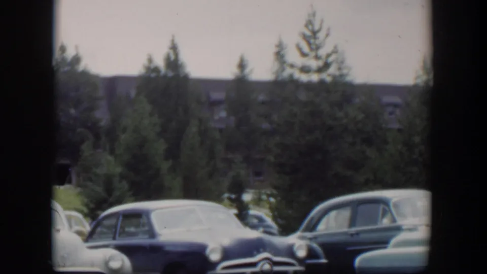 1951 Wyoming 8mm frame showing parked mid-century automobiles in a quiet lot framed by trees and soft film grain.