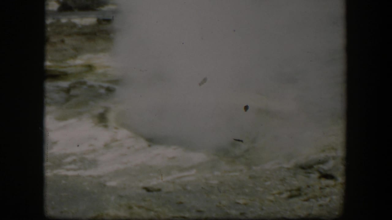 Steam rises from a pale mineral-streaked geyser vent.