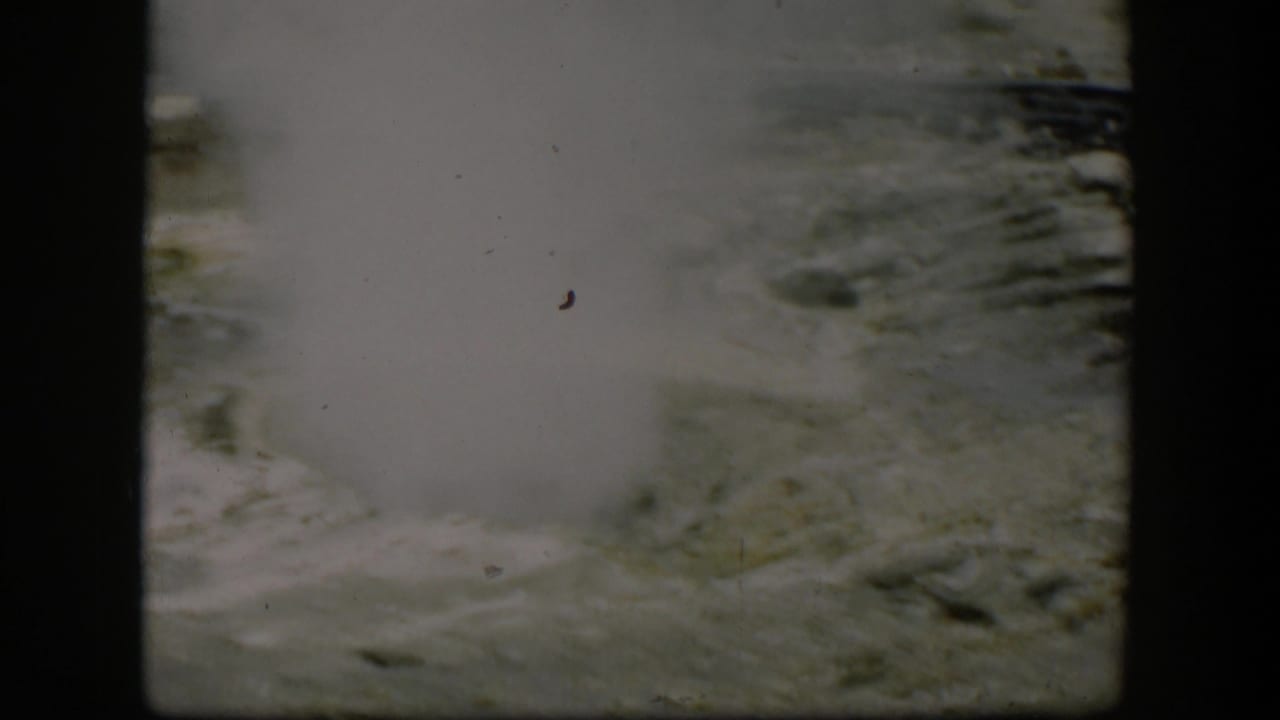 1951 Yellowstone home-movie frame with steam drifting across a pale geothermal vent and rough mineral surface.