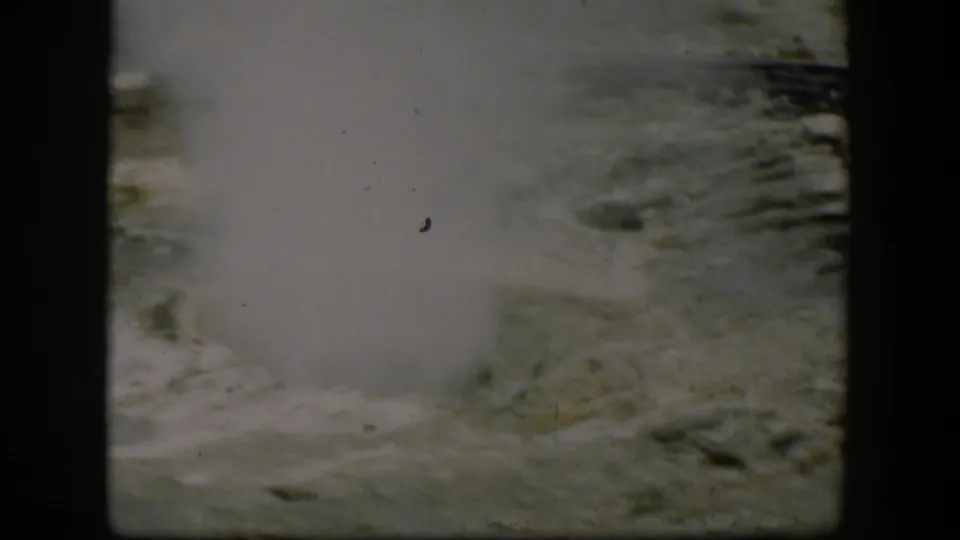 1951 Yellowstone home-movie frame with steam drifting across a pale geothermal vent and rough mineral surface.