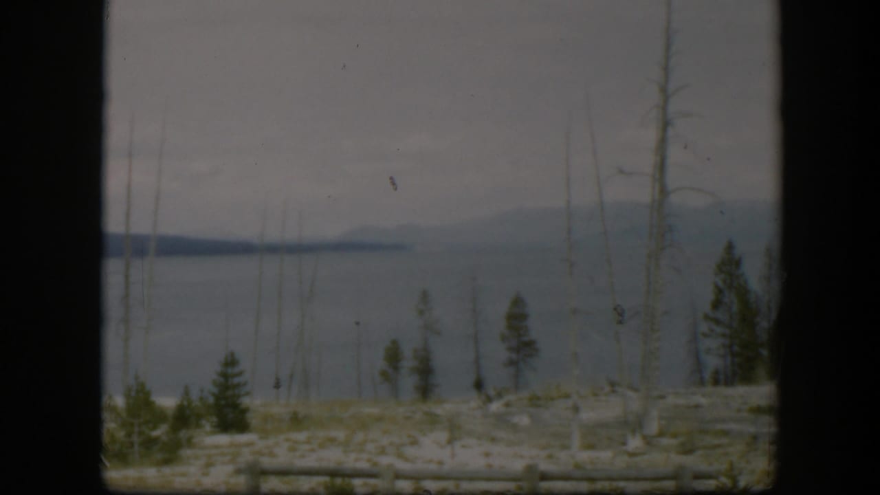 1951 Wyoming 8mm view across pale rocky ground and sparse trees toward gray-blue water and low distant hills.