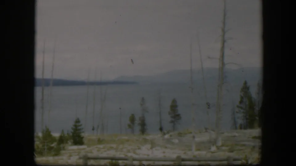 1951 Wyoming 8mm view across pale rocky ground and sparse trees toward gray-blue water and low distant hills.