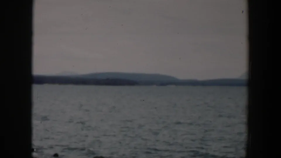 1951 Wyoming 8mm frame looking across a lake toward distant low hills beneath an overcast sky.