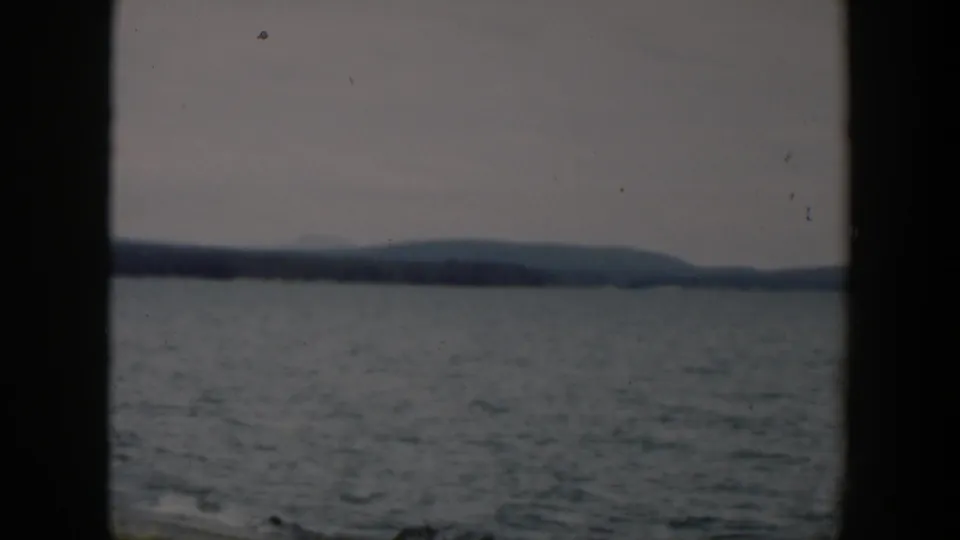 1951 Wyoming 8mm frame showing lake water, distant hills, and small dark shoreline shapes in faded color.