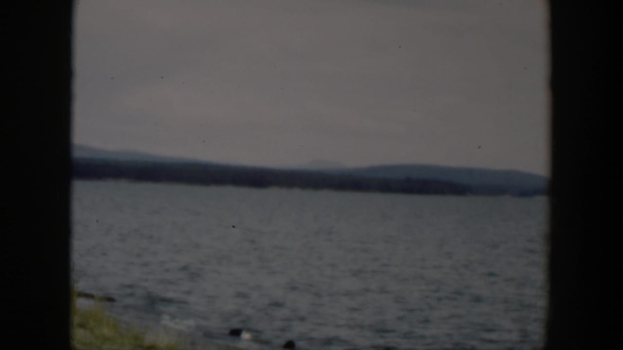 1951 Wyoming lake view with gentle surface ripples, a far wooded shore, low hills, and narrow shoreline grass at right.