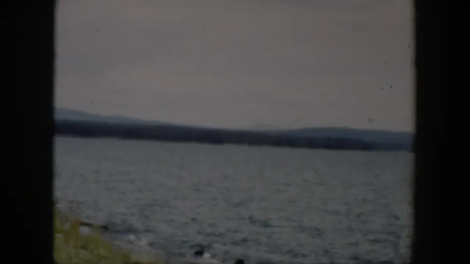 1951 Wyoming 8mm view of rippled lake water, far trees, low hills, muted sky, and a small strip of grassy shore.