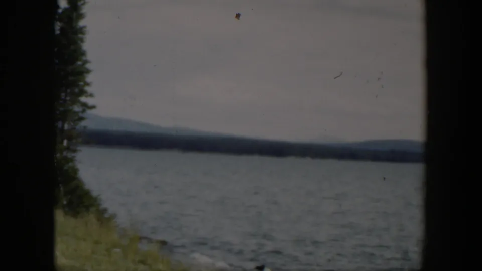 1951 Wyoming 8mm frame showing rippled lake water, a grassy shore at left, distant hills, and muted overcast sky.