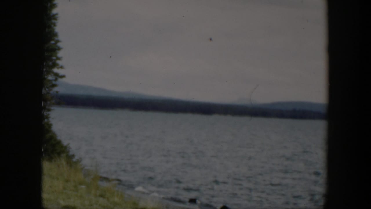 1951 Wyoming lake view with soft focus, dark frame borders, a narrow grassy bank, and low hills under gray sky.
