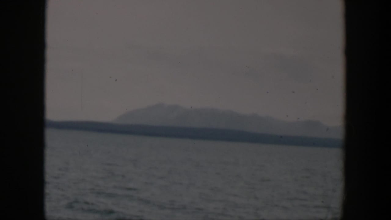 Distant mountain silhouette across gray water under an overcast sky, framed by dark vertical edges.