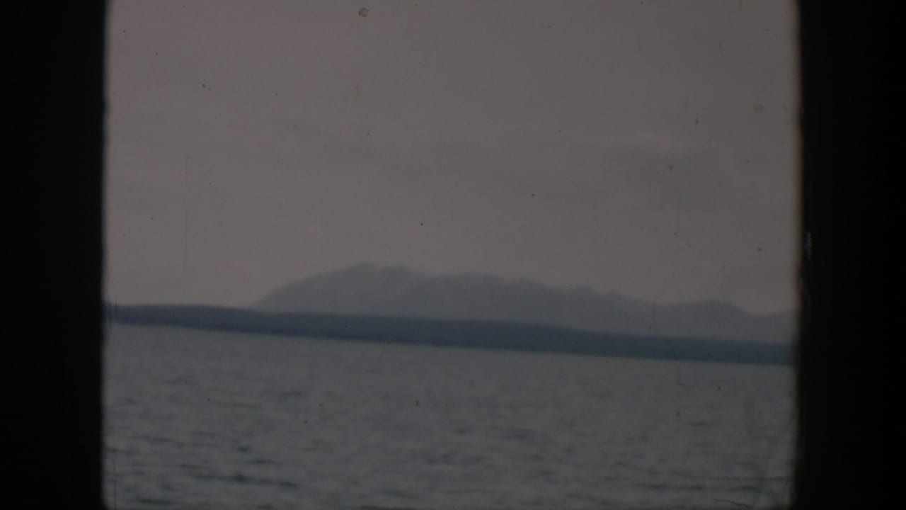 1951 Wyoming 8mm view of a pale mountain ridge and dark shoreline across gray water in overcast light.
