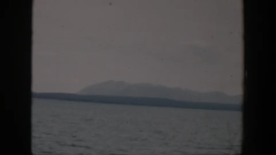 1951 Wyoming 8mm view of a pale mountain ridge and dark shoreline across gray water in overcast light.