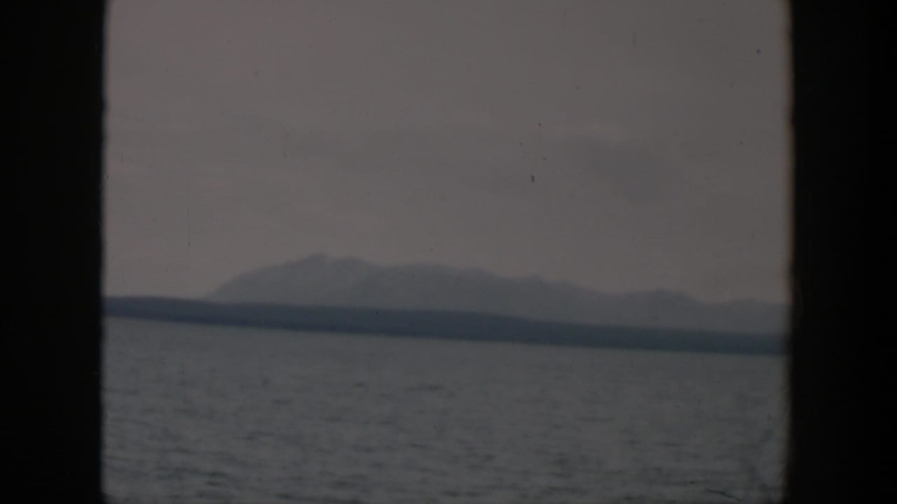 1951 Wyoming 8mm frame with a muted mountain silhouette, distant shore, and gray water under a cloudy sky.