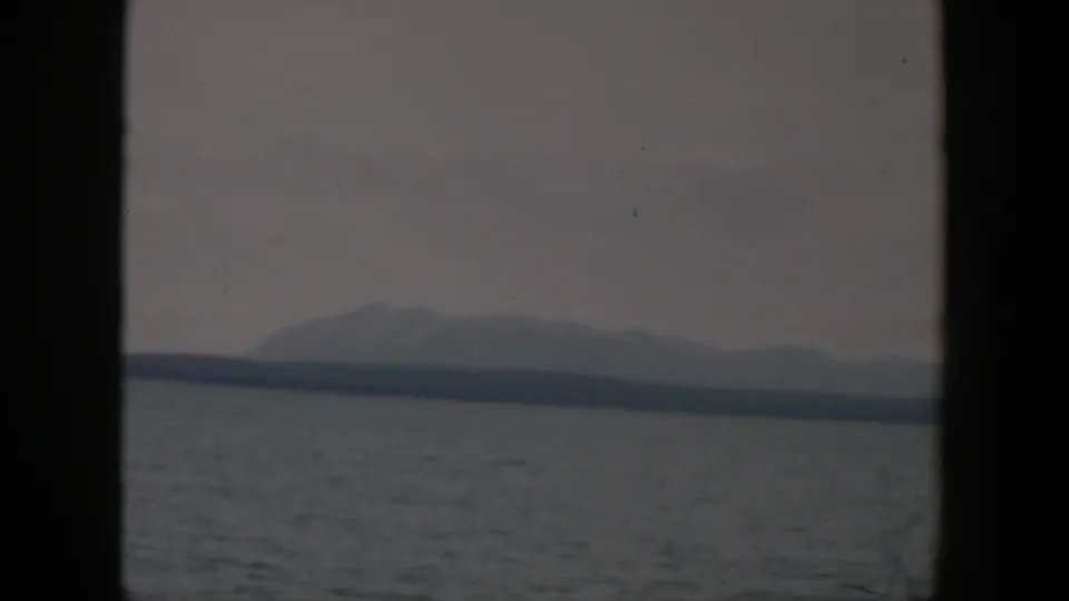 1951 Wyoming 8mm frame with a muted mountain silhouette, distant shore, and gray water under a cloudy sky.