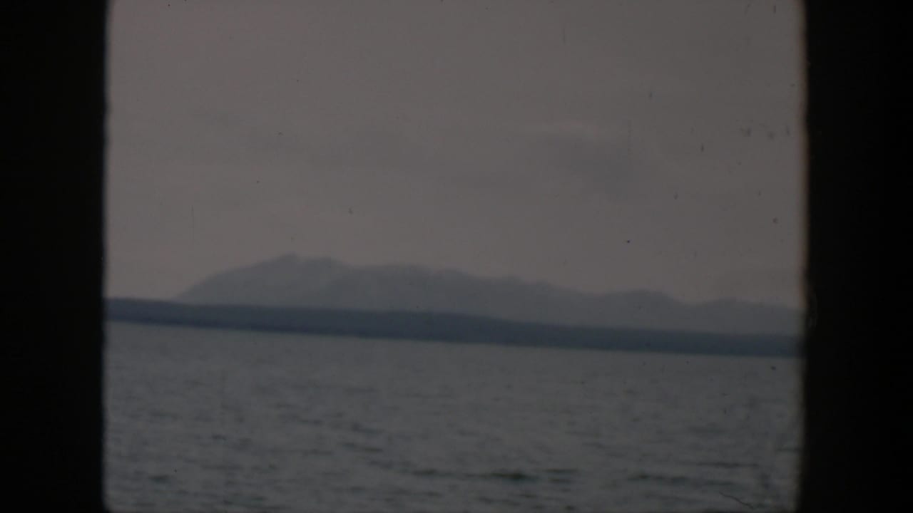 1951 Wyoming 8mm view of gray water and a distant mountain silhouette with cloudy sky and visible film texture.