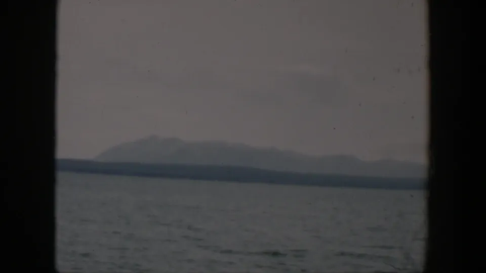 1951 Wyoming 8mm view of gray water and a distant mountain silhouette with cloudy sky and visible film texture.