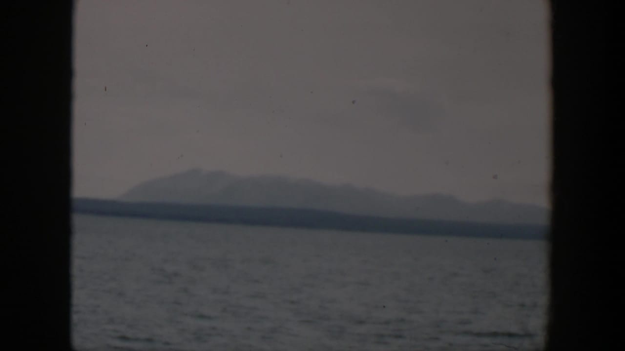 1951 8mm Wyoming home-movie frame showing open water and distant hazy mountains seen through dark window framing.
