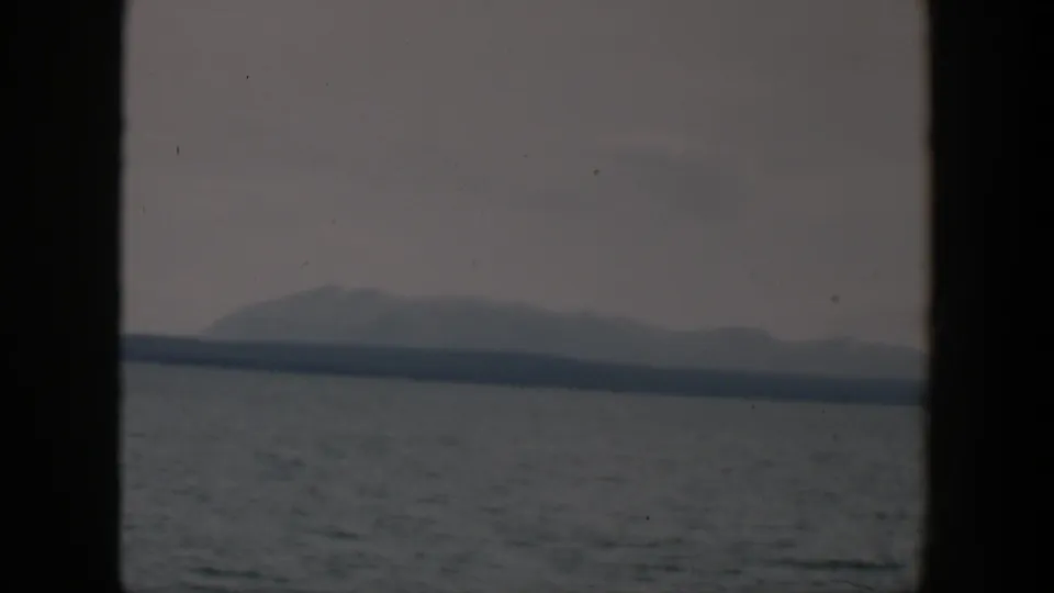 1951 8mm Wyoming home-movie frame showing open water and distant hazy mountains seen through dark window framing.