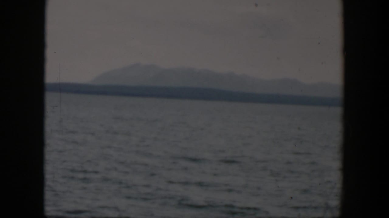 1951 8mm Wyoming view of choppy water, a low far shoreline, and hazy mountains framed by dark vertical window bars.
