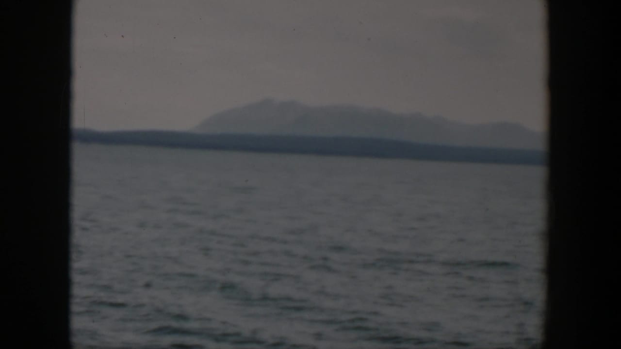 1951 8mm Wyoming landscape frame with rippling water in the foreground and a hazy mountain ridge beyond the far shore.
