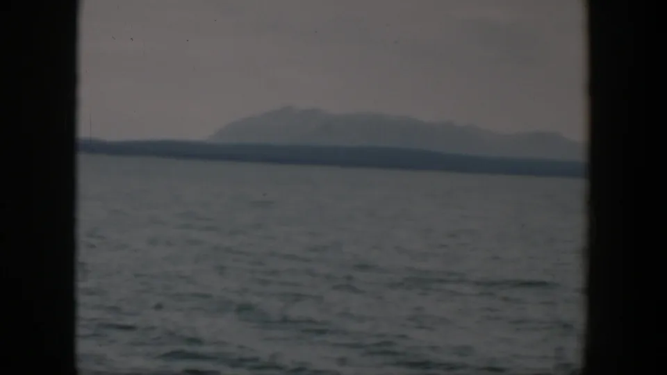 1951 8mm Wyoming landscape frame with rippling water in the foreground and a hazy mountain ridge beyond the far shore.