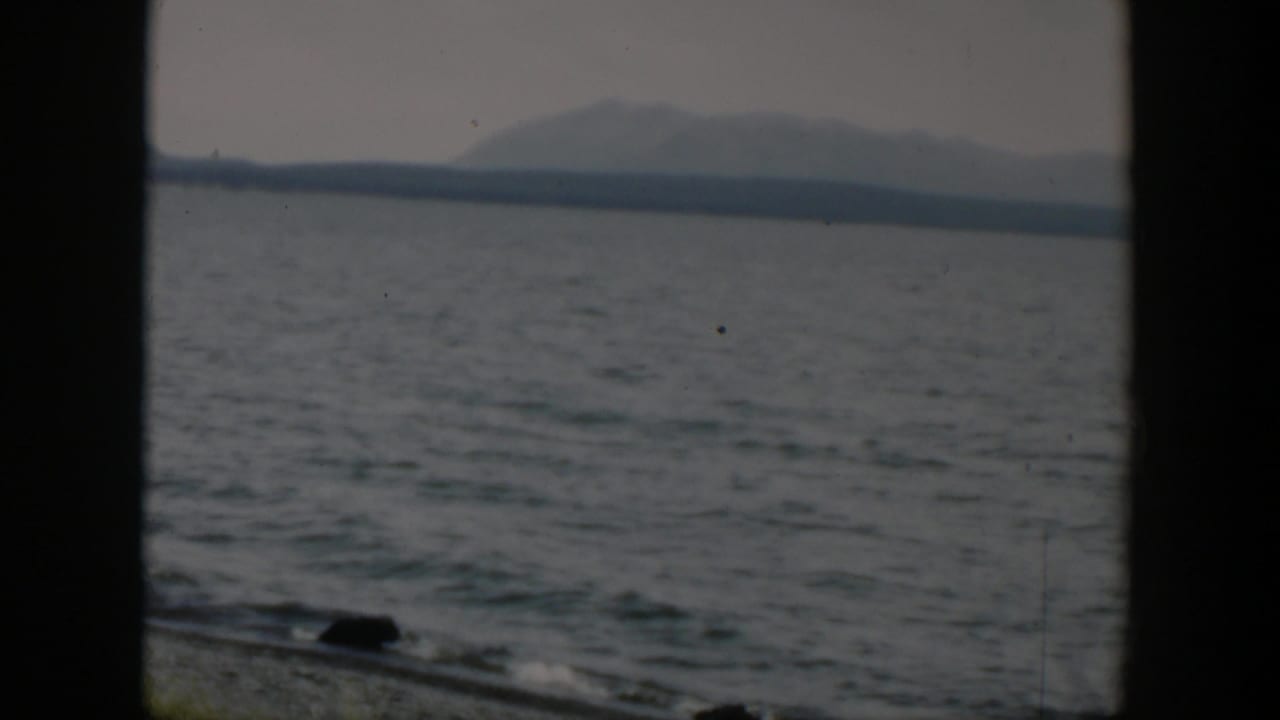 1951 8mm Wyoming frame showing open water, a distant mountain shoreline, and dark window framing near the lower edge.